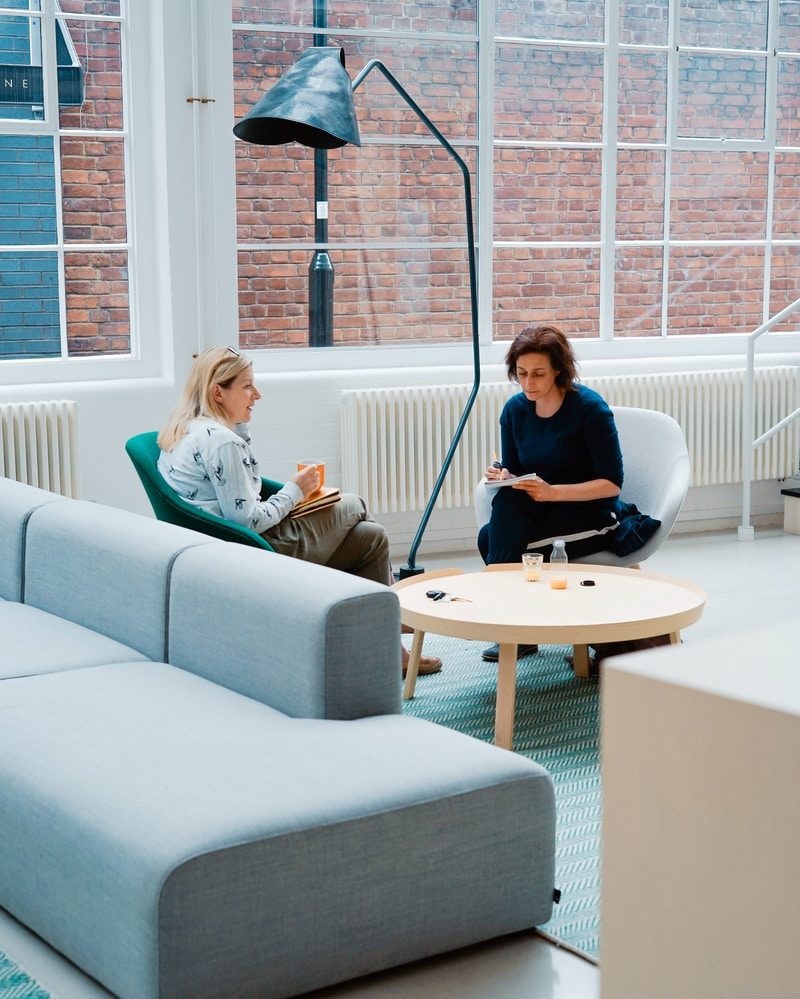 two woman sits on sofa chairs inside house